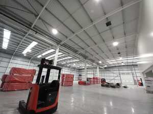 Empty warehouse interior with high ceilings and red pallets stacked in the background.