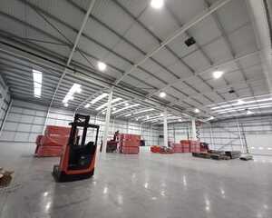 Empty industrial warehouse with a forklift and stacks of red pallets.