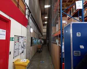 Narrow aisle in a warehouse with red walls and shelving units on one side.