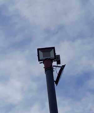 A floodlight mounted on a pole against a cloudy sky.
