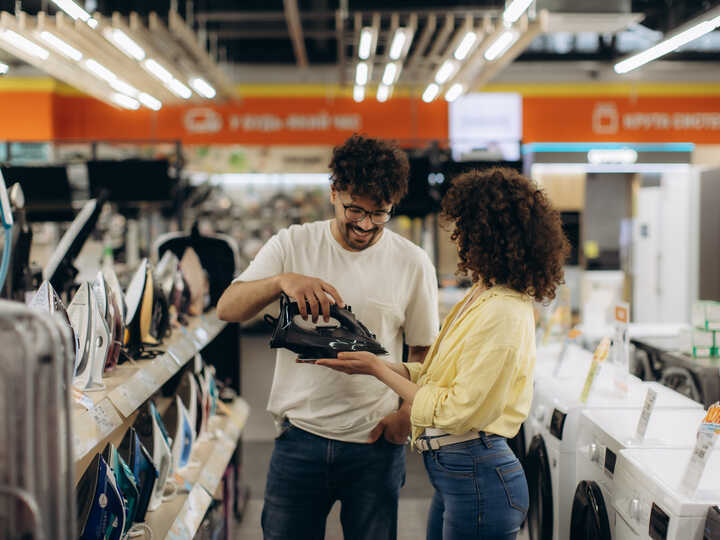 A man and woman discuss appliances in a store aisle with washing machines.