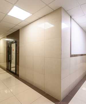 A modern corridor with tiled walls, glass door, and bright overhead lighting.
