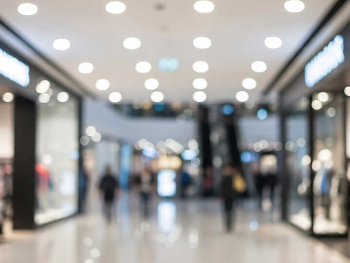 Blurred view of a shopping mall with storefronts and people walking.