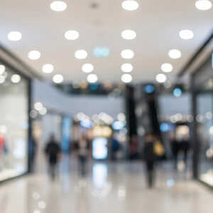 Blurred image of a shopping mall interior with stores and shoppers.