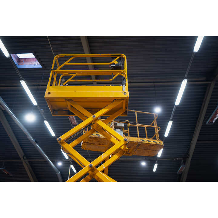 Yellow scissor lift under bright overhead lights in a warehouse.