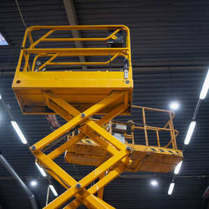 Yellow scissor lift under bright overhead lights in a warehouse.