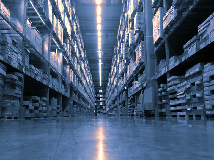 Wide aisle in a warehouse with tall shelves stacked with wooden pallets.