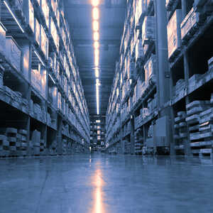 A wide angle view of a warehouse aisle with shelves stacked with pallets.