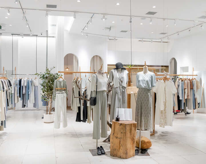 Clothing store interior with light-colored garments displayed on racks and mannequins.
