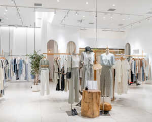 Clothing store interior with light-colored garments displayed on racks and mannequins.