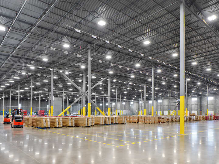 Spacious warehouse interior with bright lights and stacked pallets.
