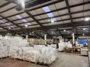 Two workers in safety vests and helmets walking through a warehouse aisle with stacked goods.