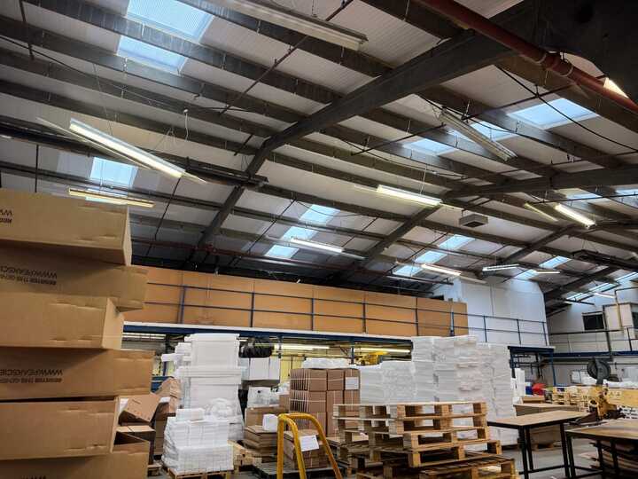 Interior of a warehouse with stacked boxes and large windows overhead.