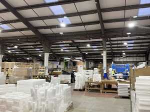 A spacious warehouse with stacks of white packaging materials and overhead lights.