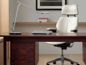 Modern office with a wooden desk, white ergonomic chair, and desk lamp.