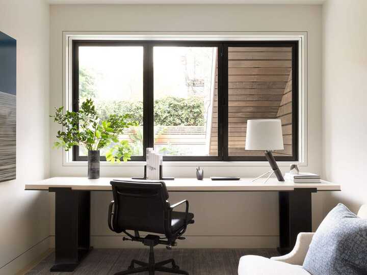 Modern home office with a desk, chair, lamp, and a view through a large window.
