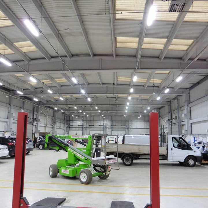 Newly lit warehouse interior with a green lift and several vehicles.